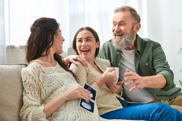 Young lgbt couple and father of one of them laughing and looking at ultrasound, ivf concept — Stock Photo