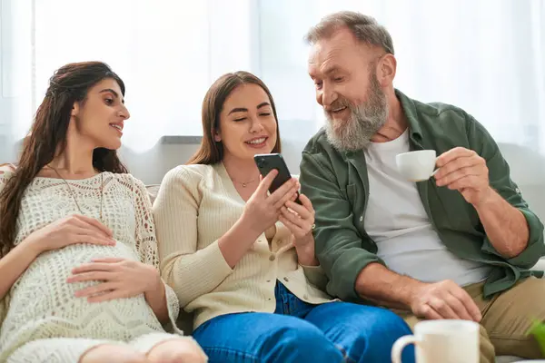 Jolly father paid visit to his daughter and her partner, on sofa looking at phone, ivf concept — Stock Photo