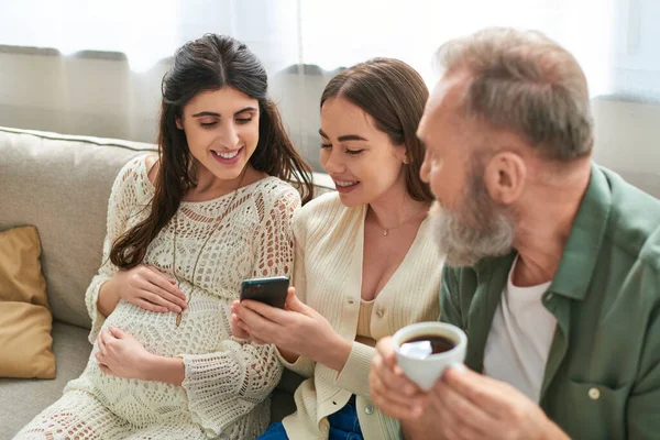 Father sitting on sofa with his pregnant daughter and her partner drinking coffee, ivf concept — Stock Photo
