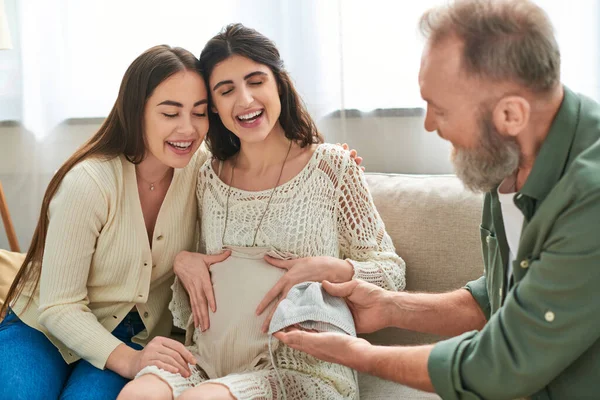 Father showing cute beanie and singlet to his pregnant daughter and her partner, ivf concept — Stock Photo