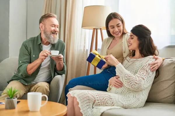 Alegre casal lésbico segurando presente e pai de um deles beber café, ivf conceito — Fotografia de Stock