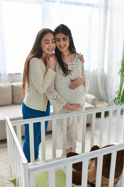 Cheerful lgbt couple hugging warmly and smiling happily standing next to crib, ivf concept — Stock Photo