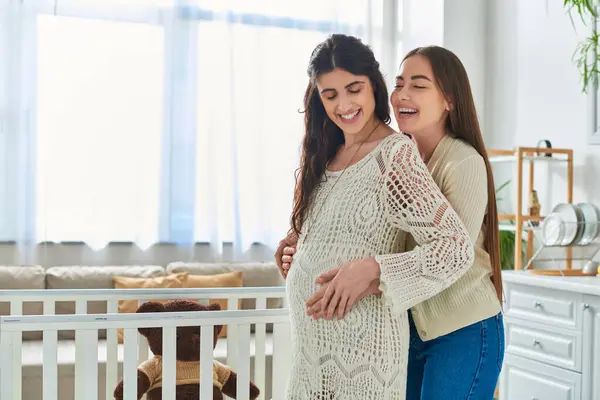Happy lesbian couple standing next to crib hugging and smiling with closed eyes, ivf concept — Stock Photo