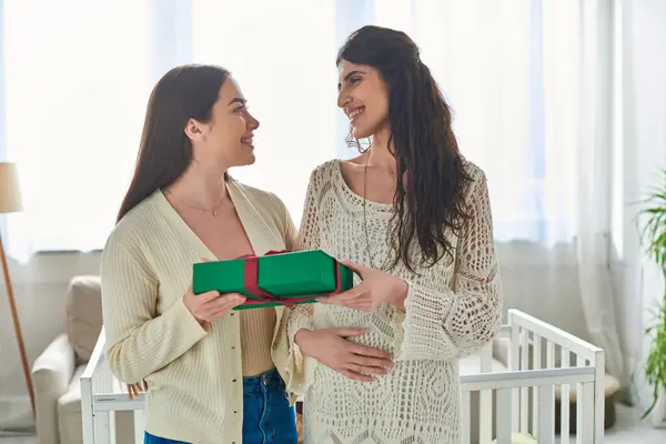 Cheerful lesbian couple holding present in hands and smiling lovingly at each other, ivf concept — Stock Photo