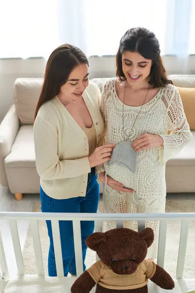 Happy expecting couple holding grey beanie and looking at teddy bear in baby crib, ivf concept — Stock Photo