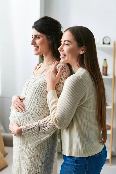Smiley expecting lesbian couple hugging warmly looking out of window, in vitro fertilisation concept — Stock Photo