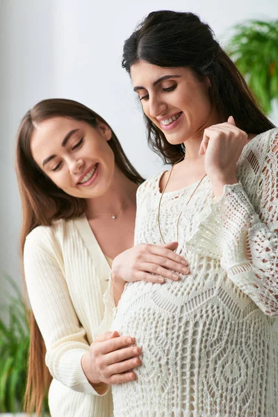 Hermosa pareja lgbt abrazando y sonriendo alegremente con las manos en el vientre embarazada, concepto ivf - foto de stock