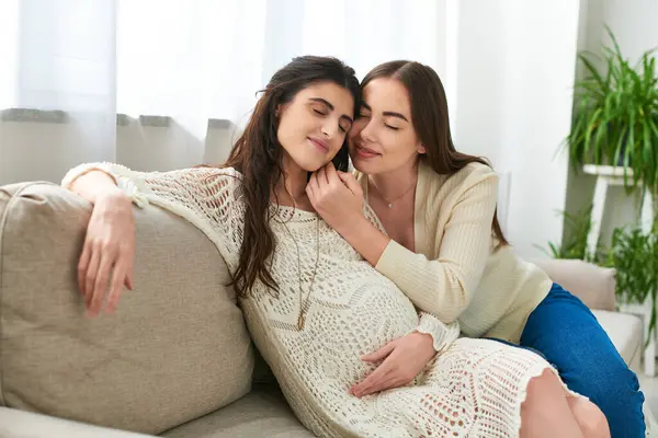 Happy lesbian couple hugging on sofa with closed eyes, hand to cheek, in vitro fertilisation concept — Stock Photo