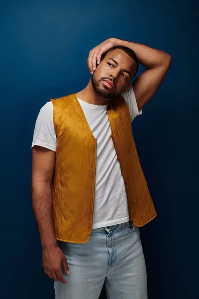 Jovem homem bonito em colete amarelo posando no fundo azul escuro colocando braço em sua cabeça, moda — Fotografia de Stock