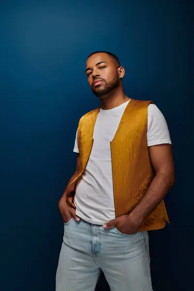 Hombre afroamericano posando sobre fondo azul oscuro con las manos en bolsillos vaqueros, concepto de moda - foto de stock