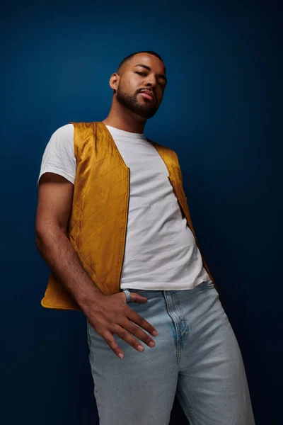 Handsome african american male model in trendy outfit posing on dark blue backdrop, fashion concept — Stock Photo