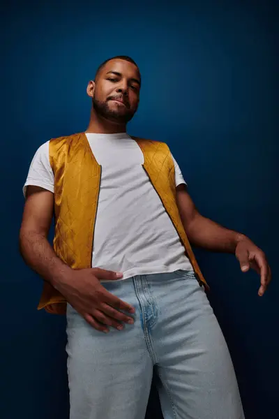 Homem bonito na moda colete amarelo olhando para a câmera posando no fundo azul escuro, conceito de moda — Fotografia de Stock