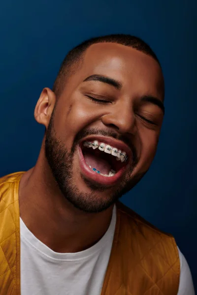 Cheerful young man with beard and braces laughing with closed eyes at camera, fashion concept — Stock Photo