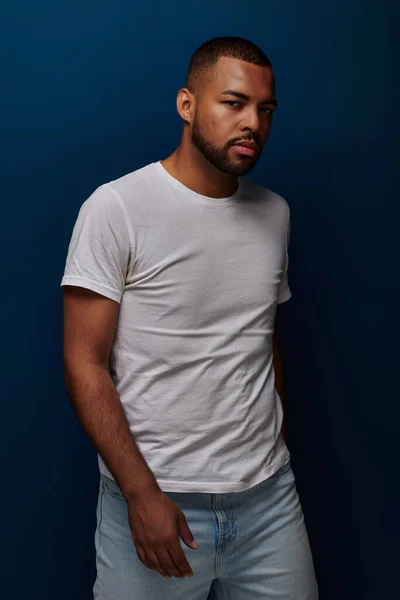 Jovem bonito em t-shirt branca e jeans posando no fundo azul olhando para longe, conceito de moda — Fotografia de Stock