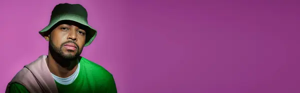 Schöner bärtiger Mann in grünem Panama vor violettem Hintergrund, der in die Kamera schaut, Modekonzept, Banner — Stockfoto