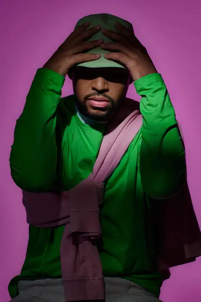 Moda giovane uomo in felpa verde posa con entrambe le mani sul suo panama, concetto di moda — Foto stock