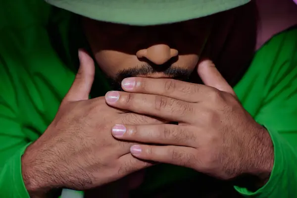 Primo piano di uomo afroamericano in panama verde con le mani sotto il mento su sfondo viola, moda — Foto stock