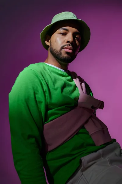 Junger gutaussehender Mann in grünem Panama mit lila Sweatshirt auf den Schultern, Modekonzept — Stockfoto