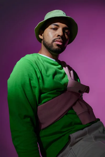 Young handsome man in green panama with purple sweatshirt tied on his shoulders, fashion concept — Stock Photo