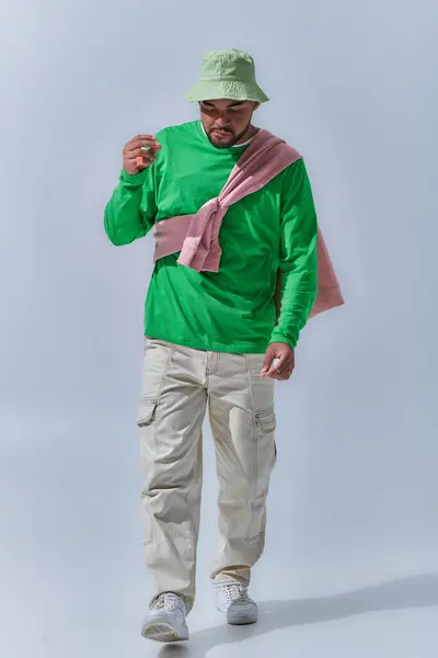 Jovem modelo masculino barbudo em camisola verde posando em movimento olhando para baixo, conceito de moda — Fotografia de Stock