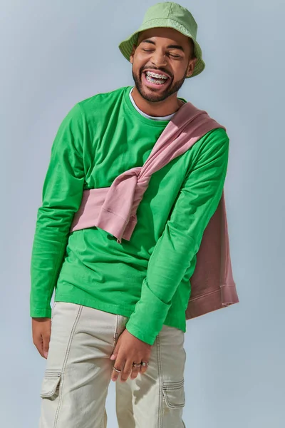 Cheerful young man in stylish outfit laughing sincerely on light blue backdrop, fashion concept — Stock Photo