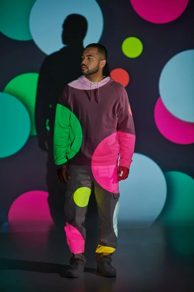 Homem bonito com capuz rosa de pé e olhando para longe em luzes de projetor digital, conceito de moda — Fotografia de Stock
