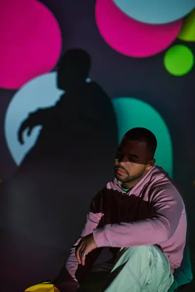 Good looking man in pink hoodie sitting on floor in digital projector lights, fashion concept — Stock Photo