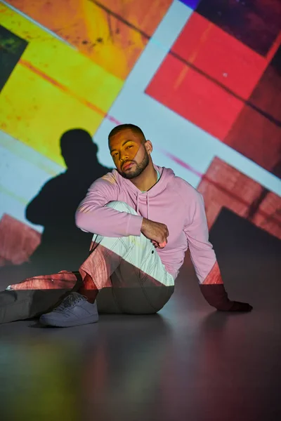 Handsome stylish man sitting on floor posing in vibrant digital projector lights, fashion concept — Stock Photo