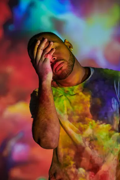 Молодий чоловік у яскравій сорочці закриває обличчя рукою в цифровому проекторі вогні, концепція моди — стокове фото