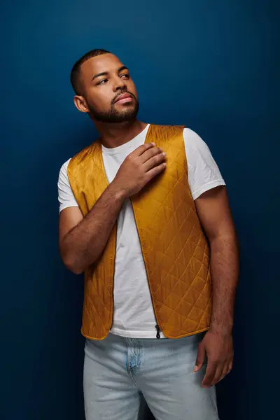 Homem afro-americano bonito em colete amarelo e mão perto do rosto olhando para longe, conceito de moda — Fotografia de Stock