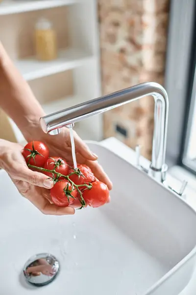 Vista recortada de la mujer lavando tomates rojos frescos de cereza en la cocina, manos femeninas y cocina casera - foto de stock