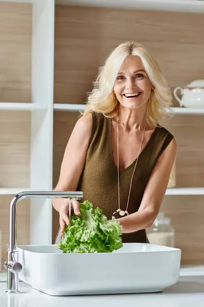 Excitée femme végétarienne d'âge moyen avec cheveux blonds lavage laitue fraîche, plan vertical — Photo de stock
