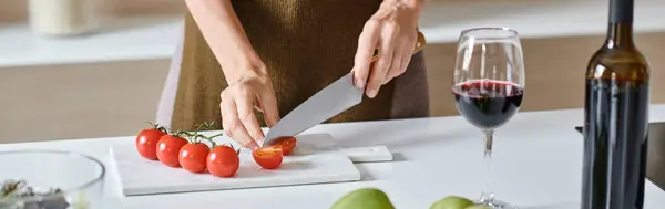 Mujer recortada cortando tomates cherry frescos cerca de un vaso de vino tinto, aguacate y manzanas verdes, pancarta - foto de stock