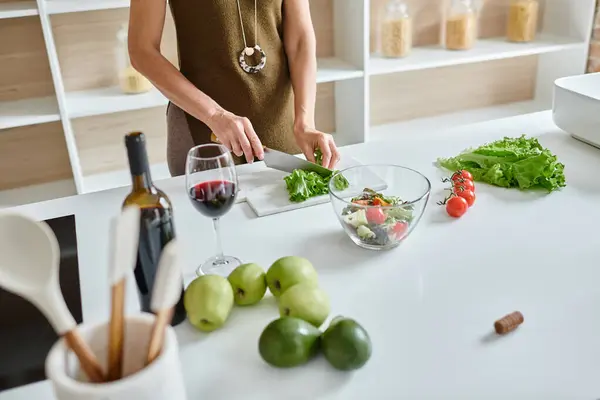 Teilaufnahme einer Frau, die frischen Salat schneidet und Gemüsesalat in der Nähe eines Rotweinglases zubereitet — Stockfoto