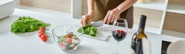 Abgeschnittenes Banner einer Frau, die frischen Salat schneidet und Gemüsesalat in der Nähe eines Rotweinglases zubereitet — Stockfoto