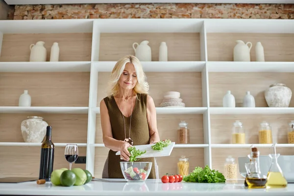 Mulher de meia idade atraente fazendo salada de ingredientes frescos na cozinha moderna, cozinhar em casa — Fotografia de Stock