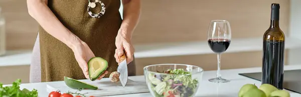 Cropped banner, woman cutting ripe avocado near fresh ingredients and red wine, home cooking — Stock Photo