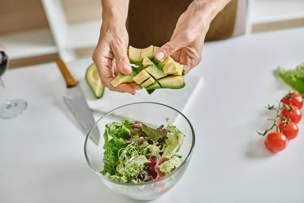 Cropped woman holding sliced ripe avocado near lettuce in bowl and glass of red wine, close up — Stock Photo