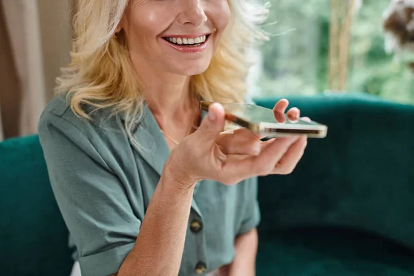 Abgeschnittene Ansicht einer glücklichen blonden Frau mittleren Alters, die eine Sprachmassage auf ihrem Smartphone aufzeichnet — Stockfoto