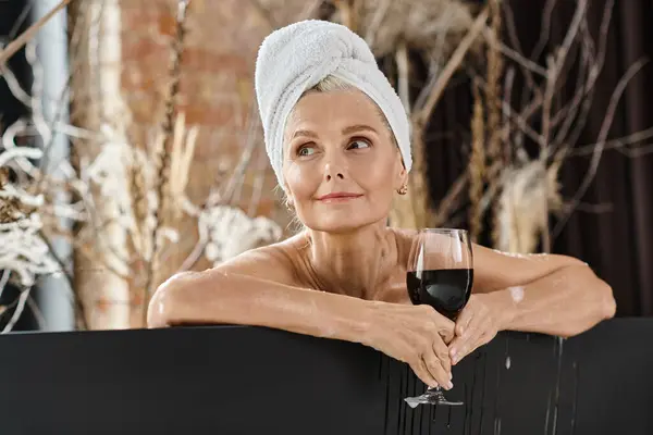 Relaxed middle aged woman with towel on head holding glass of red wine while taking bath at home — Stock Photo