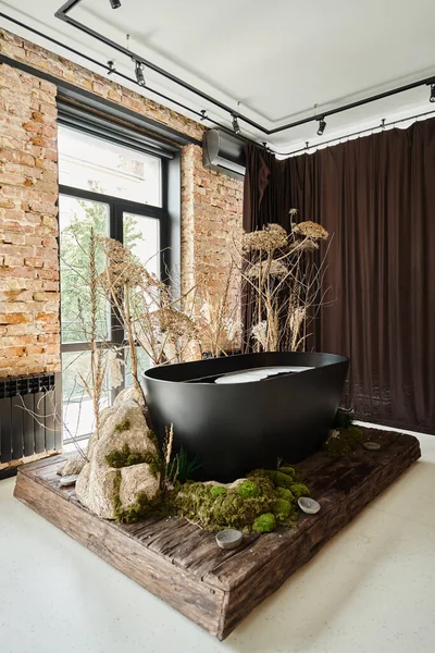 Black bathtub inside of modern apartment with panoramic windows and decorative plants and mold — Stock Photo