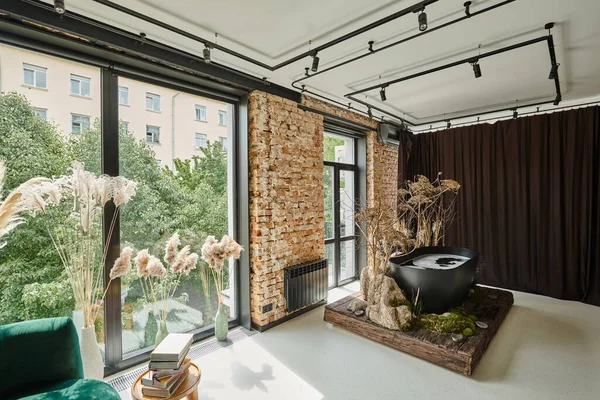 Schwarze Badewanne in einer modernen Wohnung mit Büchern auf Couchtisch, Panoramafenstern und Pflanzen — Stockfoto