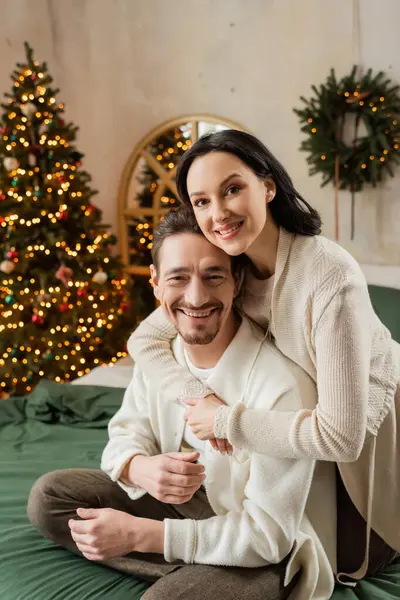 Mulher feliz abraçando marido barbudo perto de árvore de Natal borrada no apartamento moderno, contentamento — Fotografia de Stock