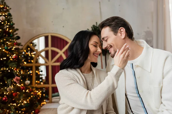 Happy woman touching gently face of husband near blurred Christmas tree in apartment, season of joy — Stock Photo