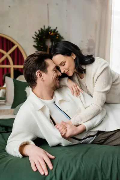 Feliz casal deitado juntos na cama perto turva grinalda de Natal na parede, temporada de alegria — Fotografia de Stock