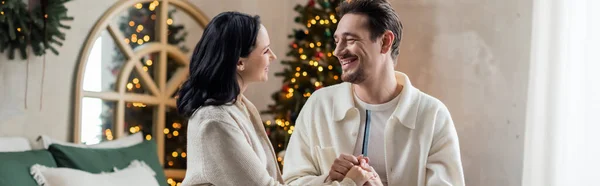 Estandarte de feliz pareja en el hogar llevar de la mano y mirarse el uno al otro cerca del árbol de Navidad - foto de stock