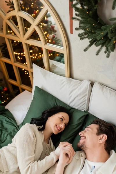 Vista superior de la alegre pareja casada pasando la acogedora mañana de Navidad y mirándose en la cama - foto de stock