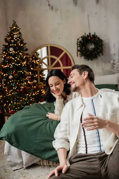 Temporada de alegria, homem feliz conversando com a esposa perto da árvore de Natal decorada no quarto moderno — Fotografia de Stock