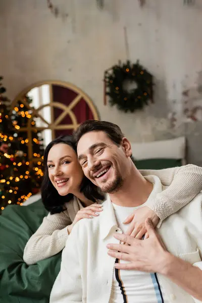 Stechpalme fröhliche Weihnachten, glückliche Frau umarmt Ehemann und verbringt Zeit zusammen im modernen Schlafzimmer — Stockfoto