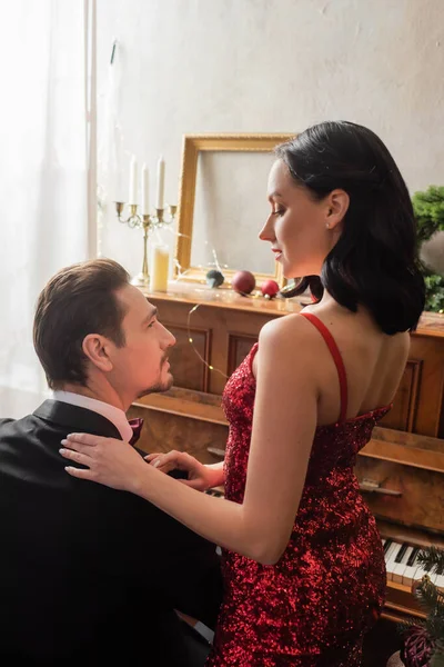 Couple riche, belle femme en robe rouge debout à côté du mari en smoking et piano — Photo de stock